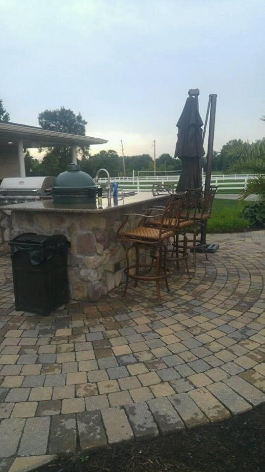 A patio with a grill, chairs, umbrellas and a trash can.