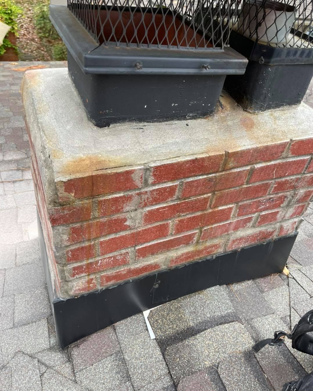 A brick chimney on top of a roof with trees in the background.