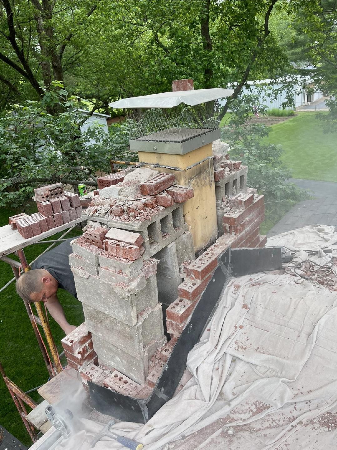 A man is working on a brick chimney on a scaffolding.