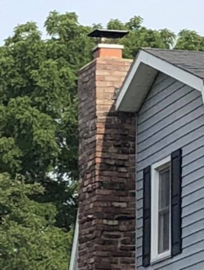 A brick chimney on the side of a house with trees in the background.