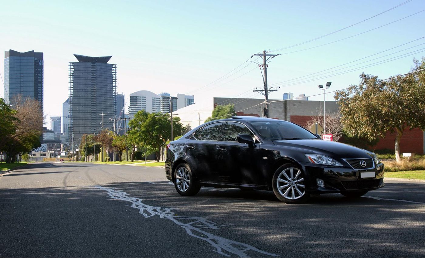 A black car is parked on the side of the road in front of a city skyline.