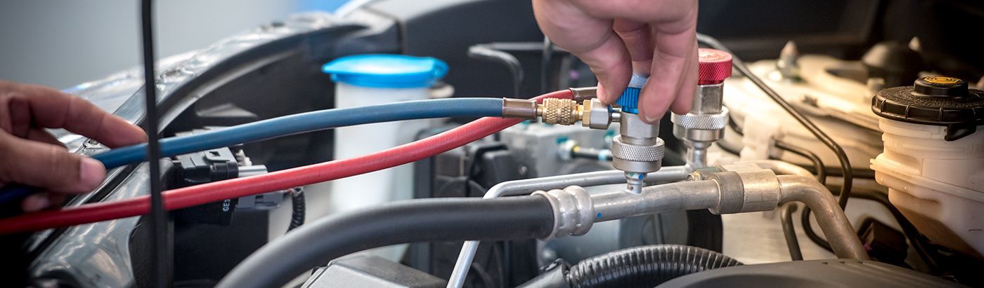 Hands adjusting a metal valve on engine hoses in a car engine bay