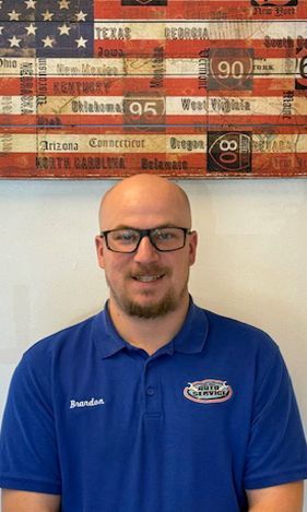 Man with glasses and blue polo shirt smiles, in front of an American flag made of license plates.