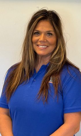 Woman with long highlighted hair wearing a blue polo shirt, smiling at the camera.
