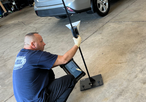 A man is kneeling down in a garage holding a mop and a tablet.
