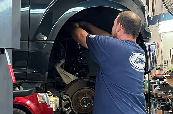 A man in a blue shirt is working on a car in a garage.