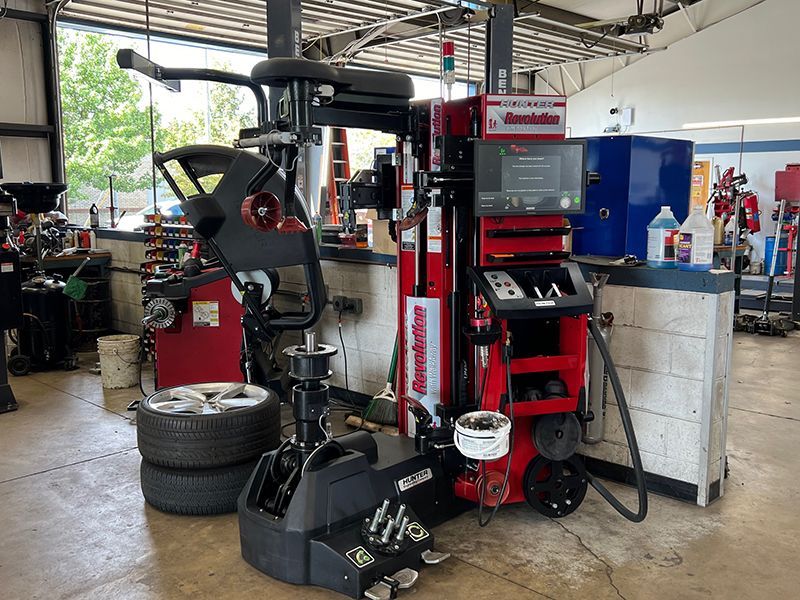 A tire balancing machine is sitting in a garage next to a stack of tires.