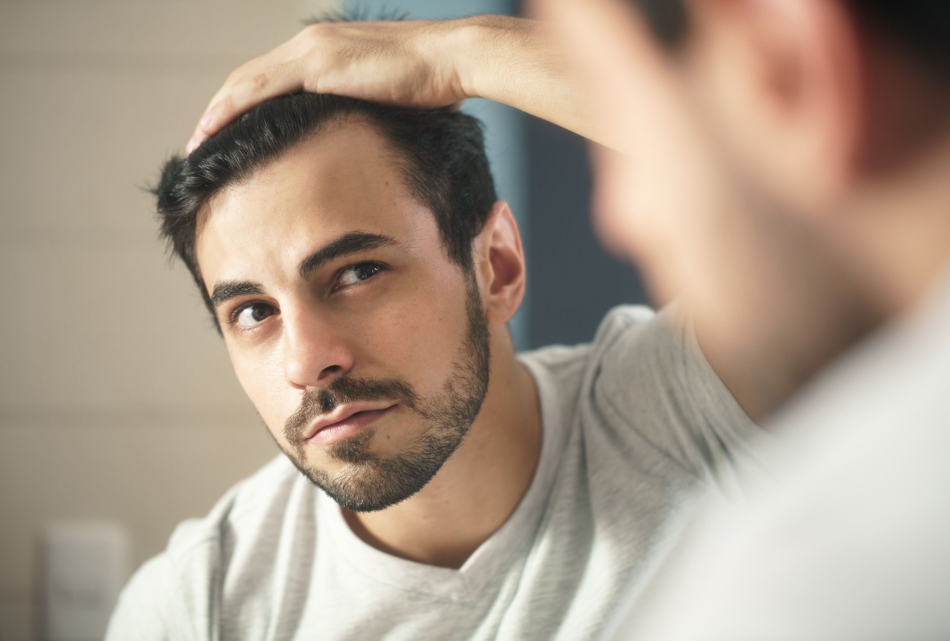 A man is looking at his hair in the mirror.