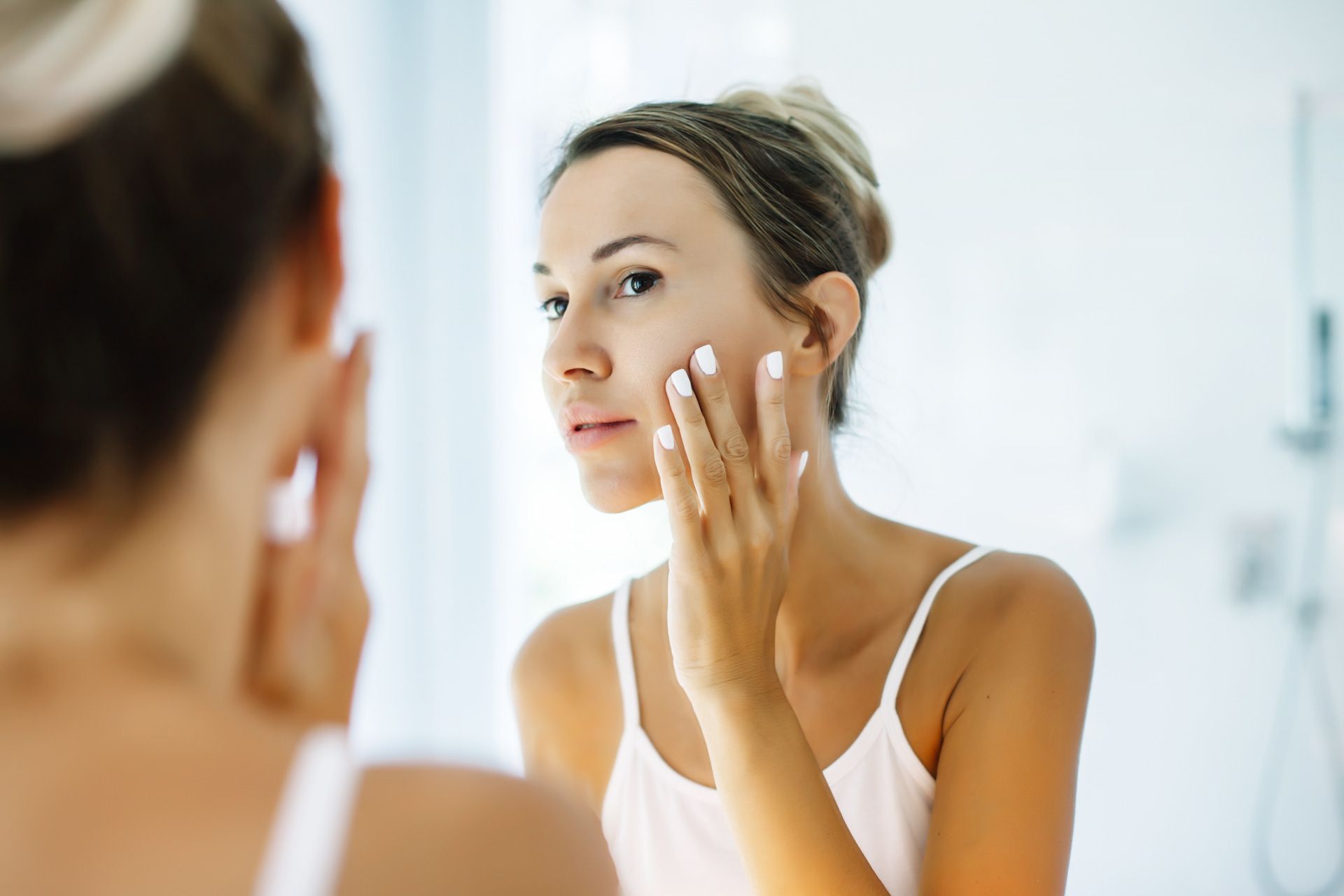 A woman is looking at her face in the mirror.