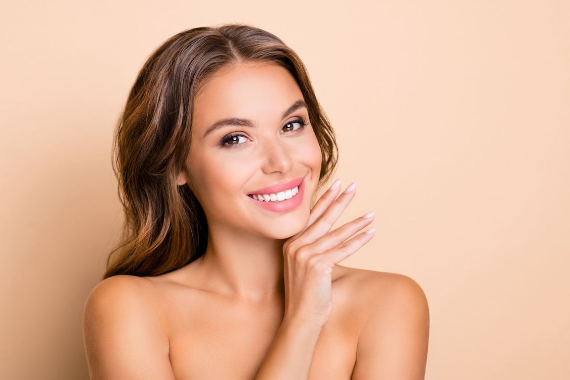 A woman is smiling and touching her face with her hand.
