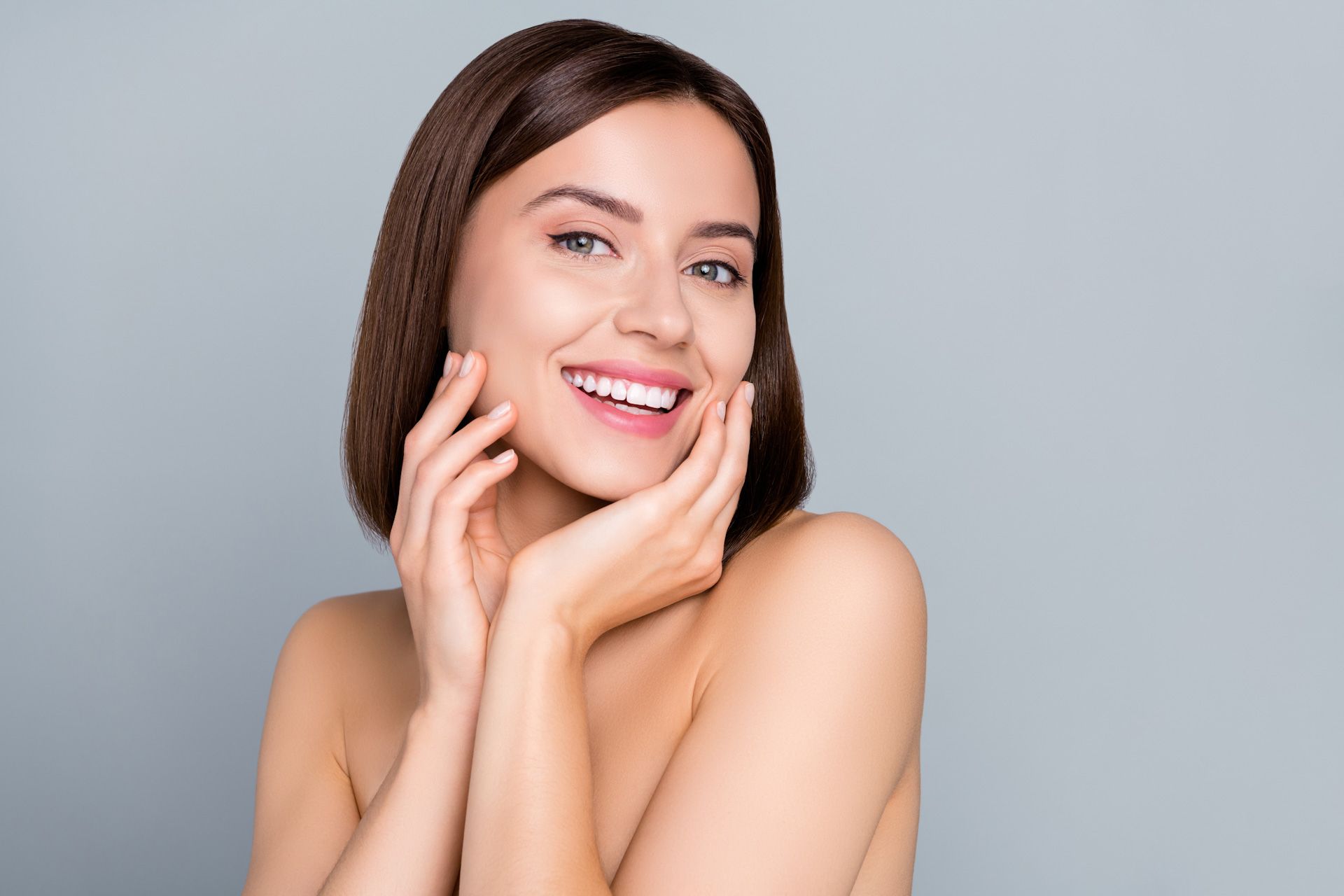 A woman is smiling and touching her face with her hands.