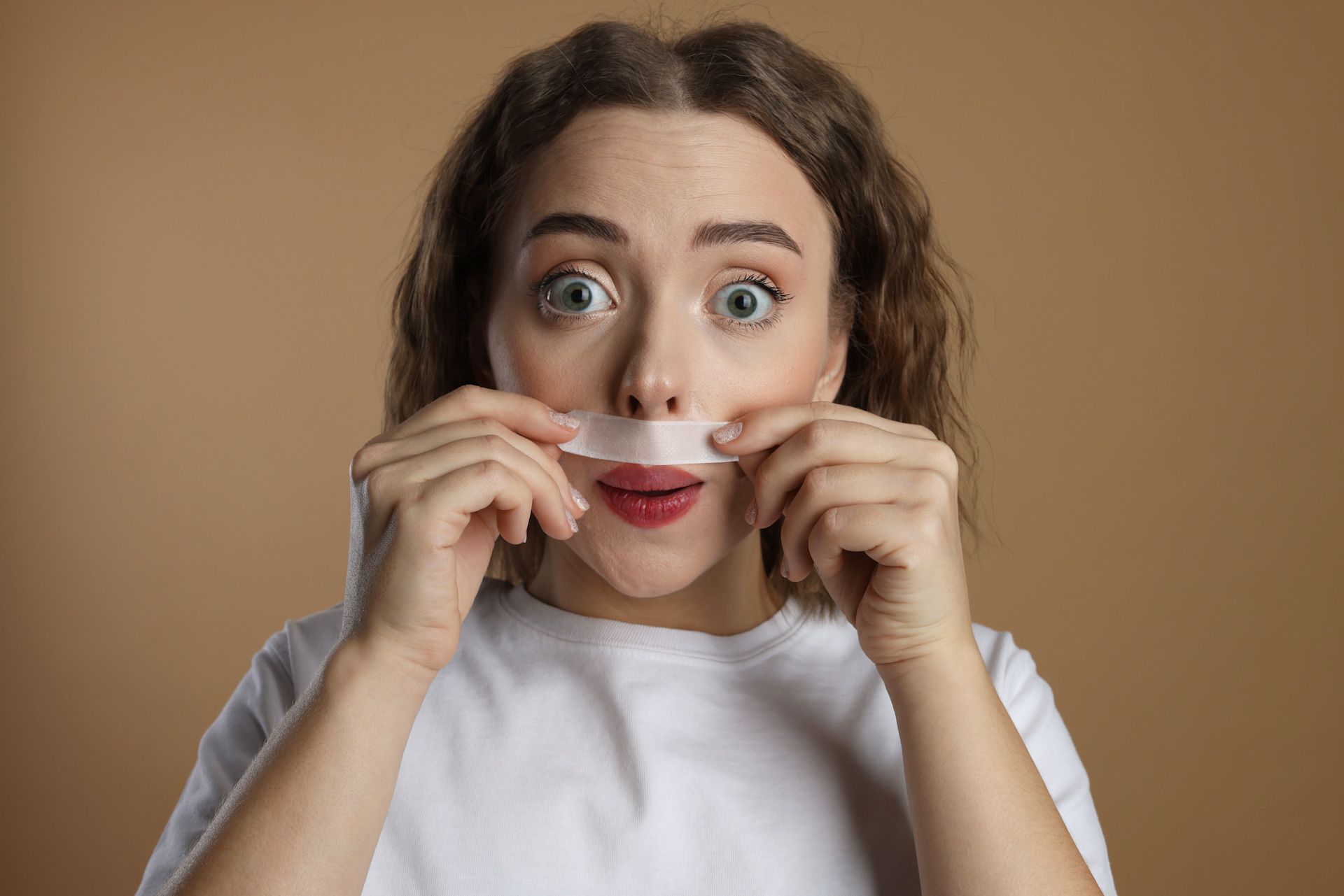 A woman is holding a piece of tape over her mouth.