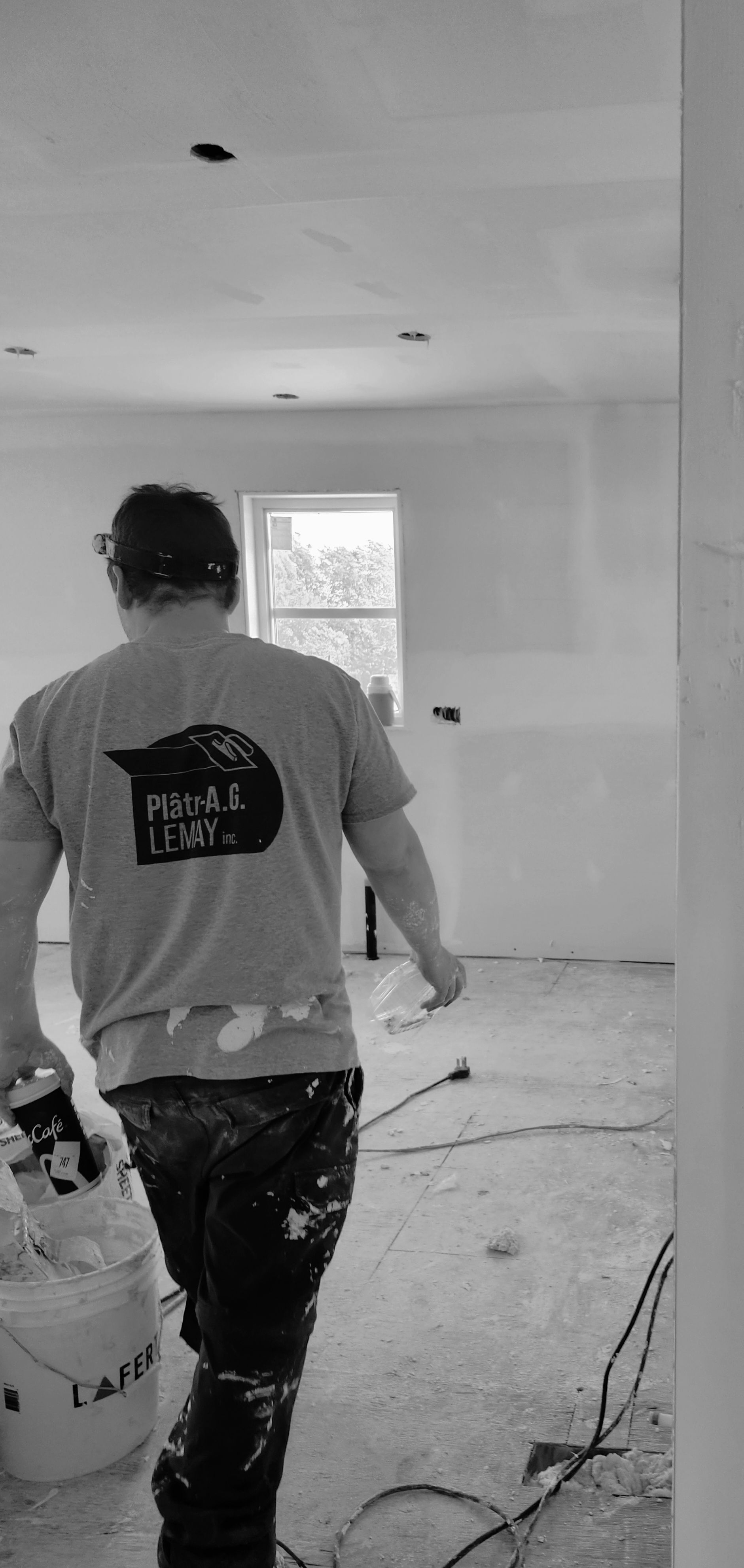 Un homme marche dans une pièce en tenant un seau de peinture.