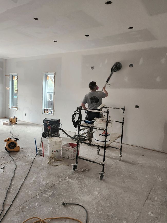 Une personne enduit un mur avec une truelle sur une photo en noir et blanc.