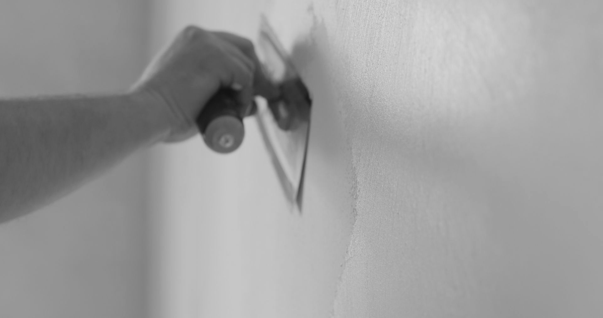 Une personne enduit un mur avec une truelle sur une photo en noir et blanc.