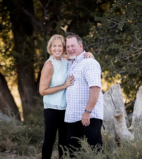 A man and a woman are posing for a picture in the woods.