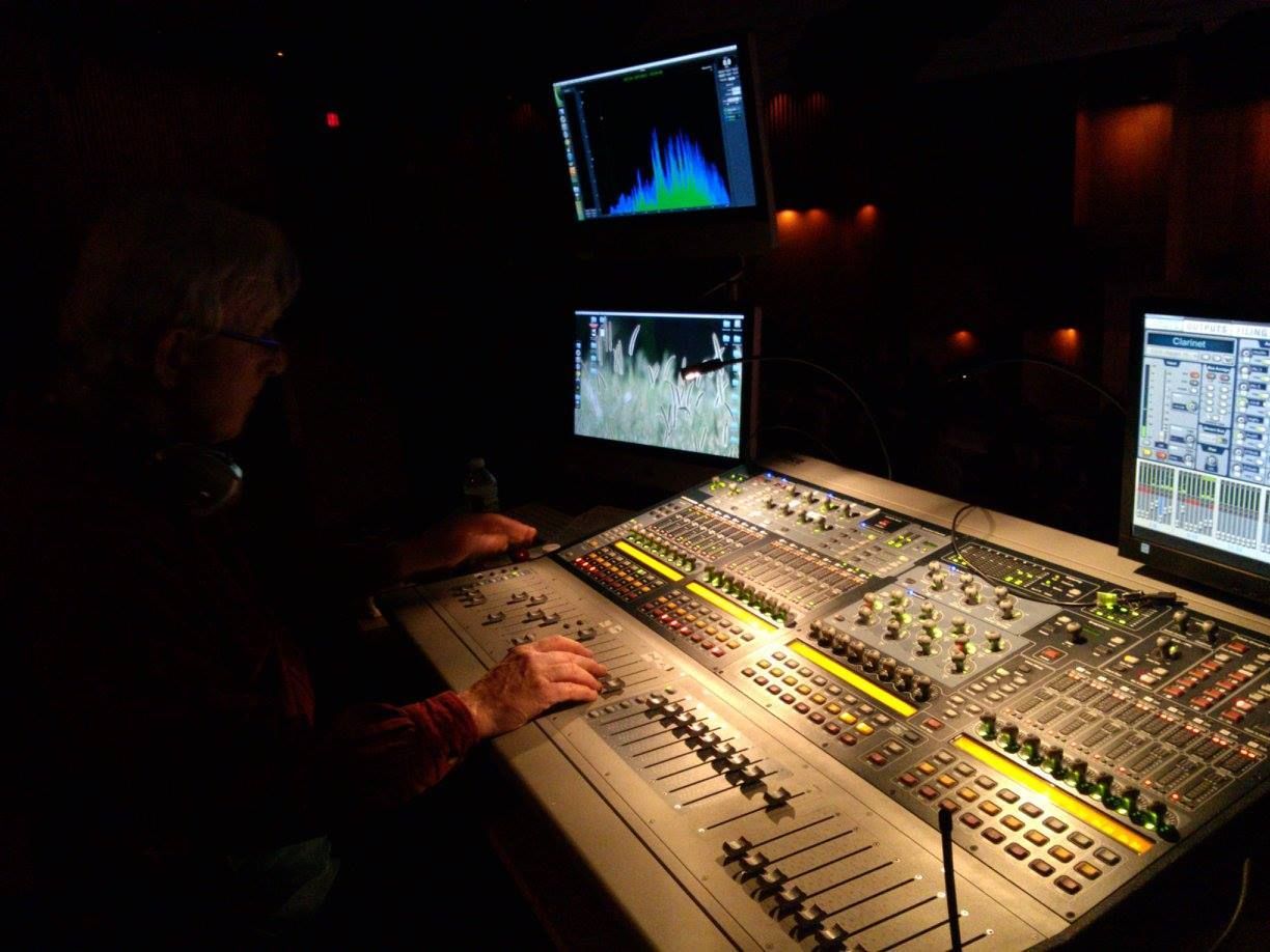 Sound engineer at a mixing console in a dark studio with illuminated monitors and controls