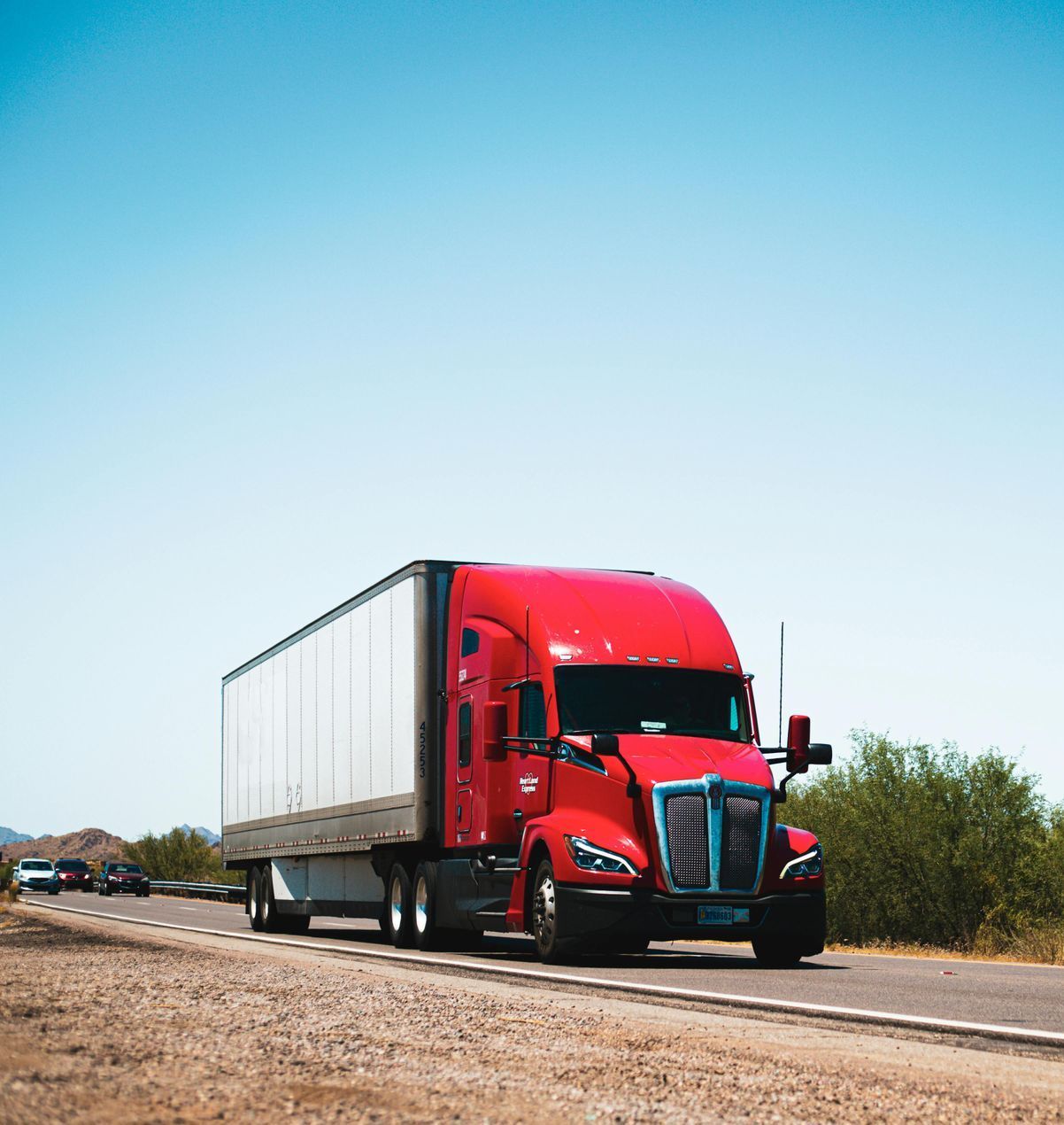 A red semi truck is driving down a dirt road.