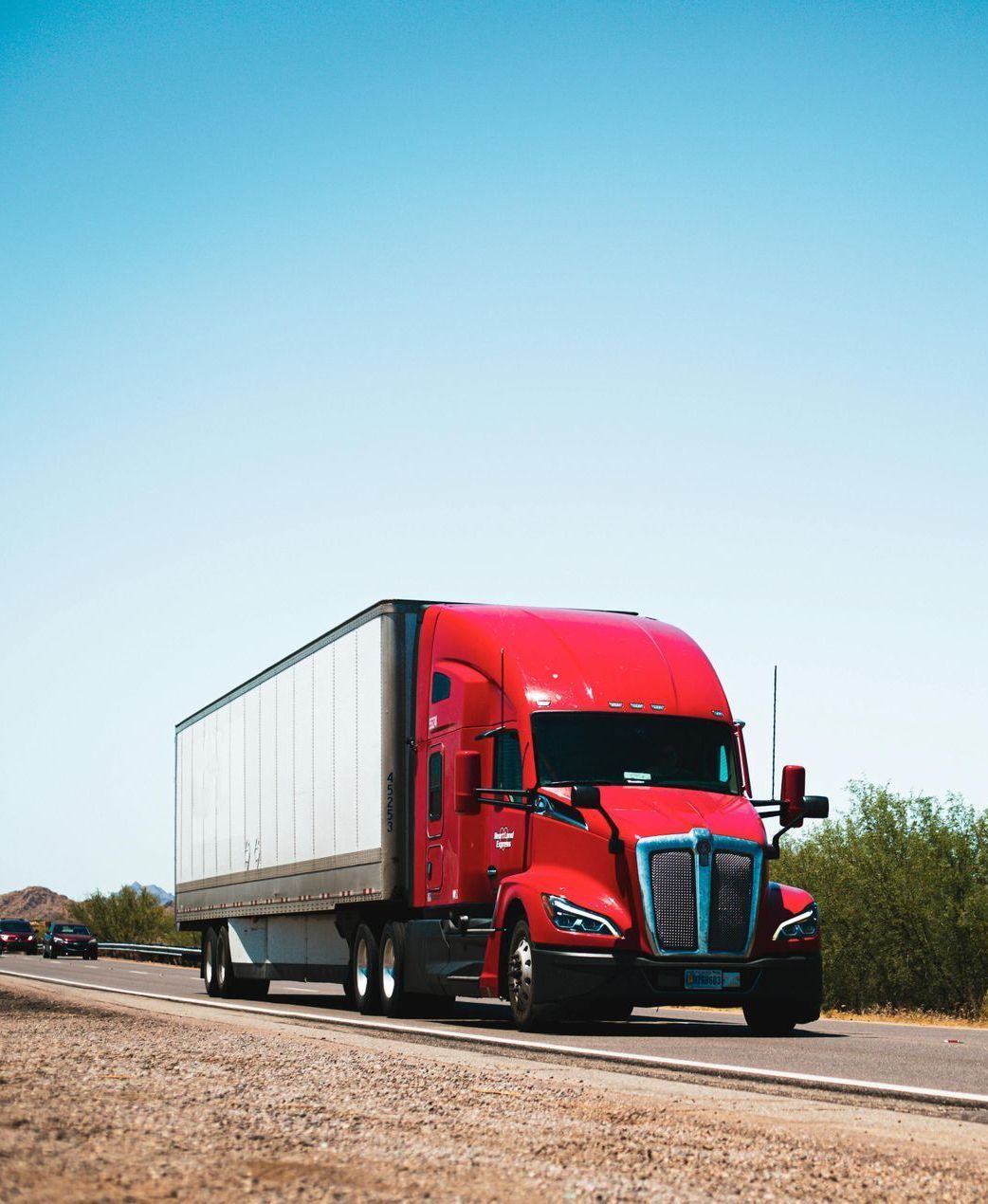 A red semi truck is driving down a dirt road.