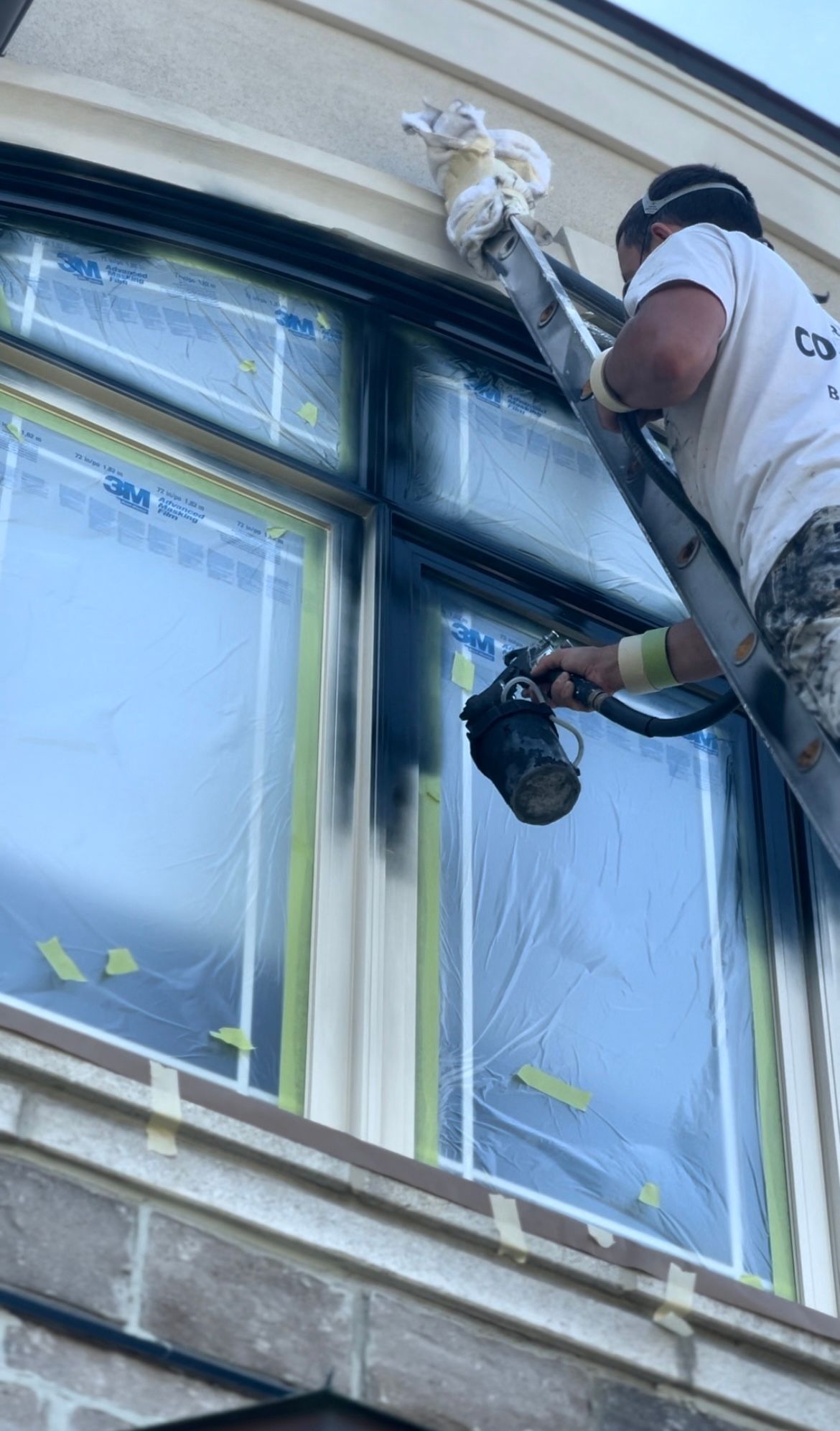 a man is standing on a ladder painting a window on a building .