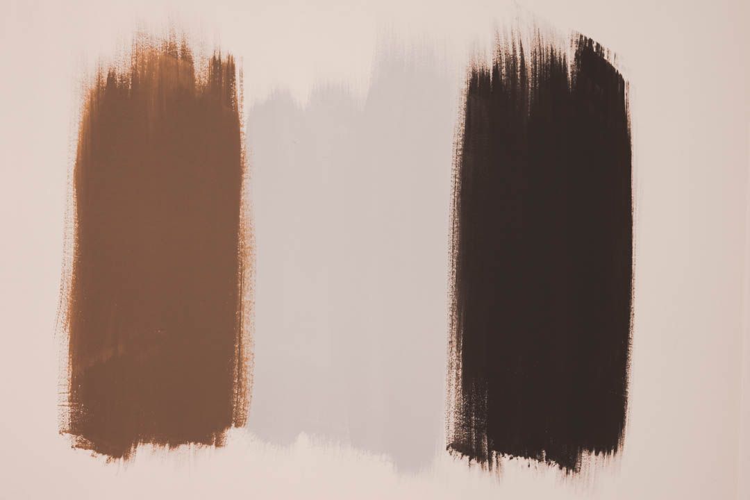 two brush strokes of brown and black paint on a white surface .