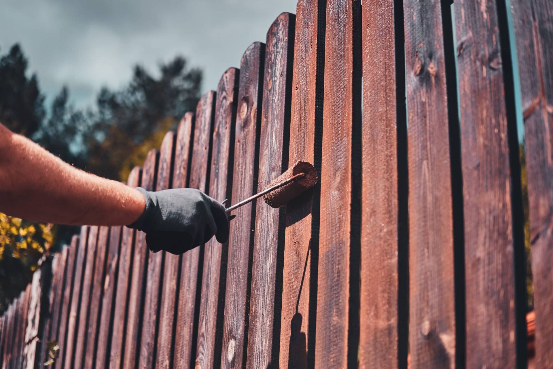 A person is painting a wooden fence with a brush.