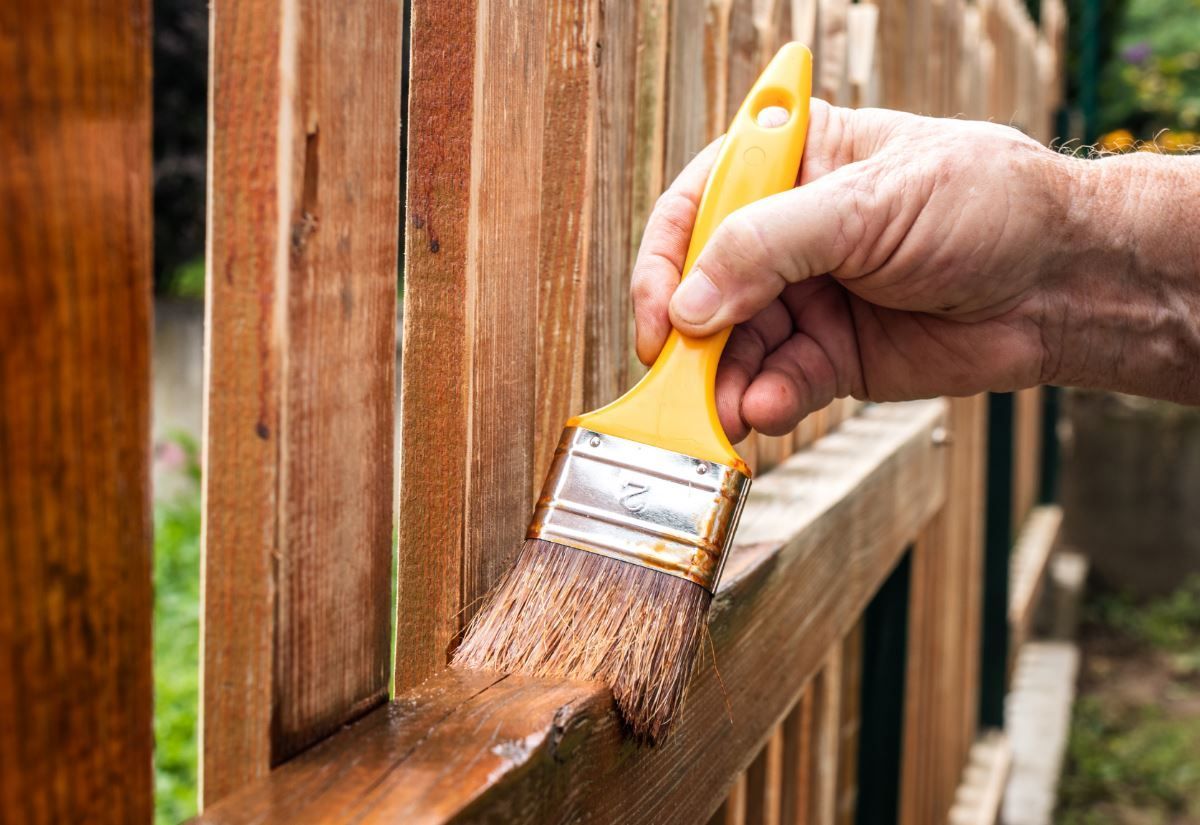 A person is painting a wooden fence with a brush.