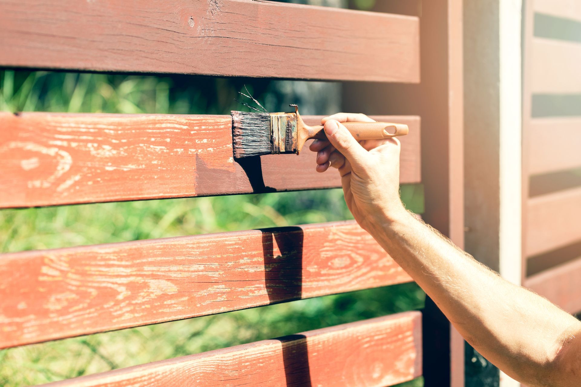 A person is painting a wooden fence with a brush.