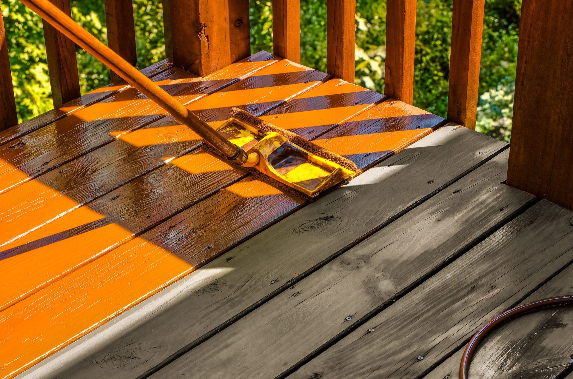 A person is painting a wooden deck with a mop.