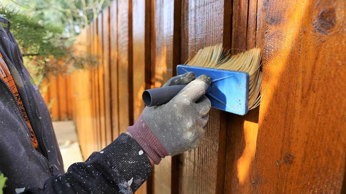 A person is painting a wooden fence with a brush.