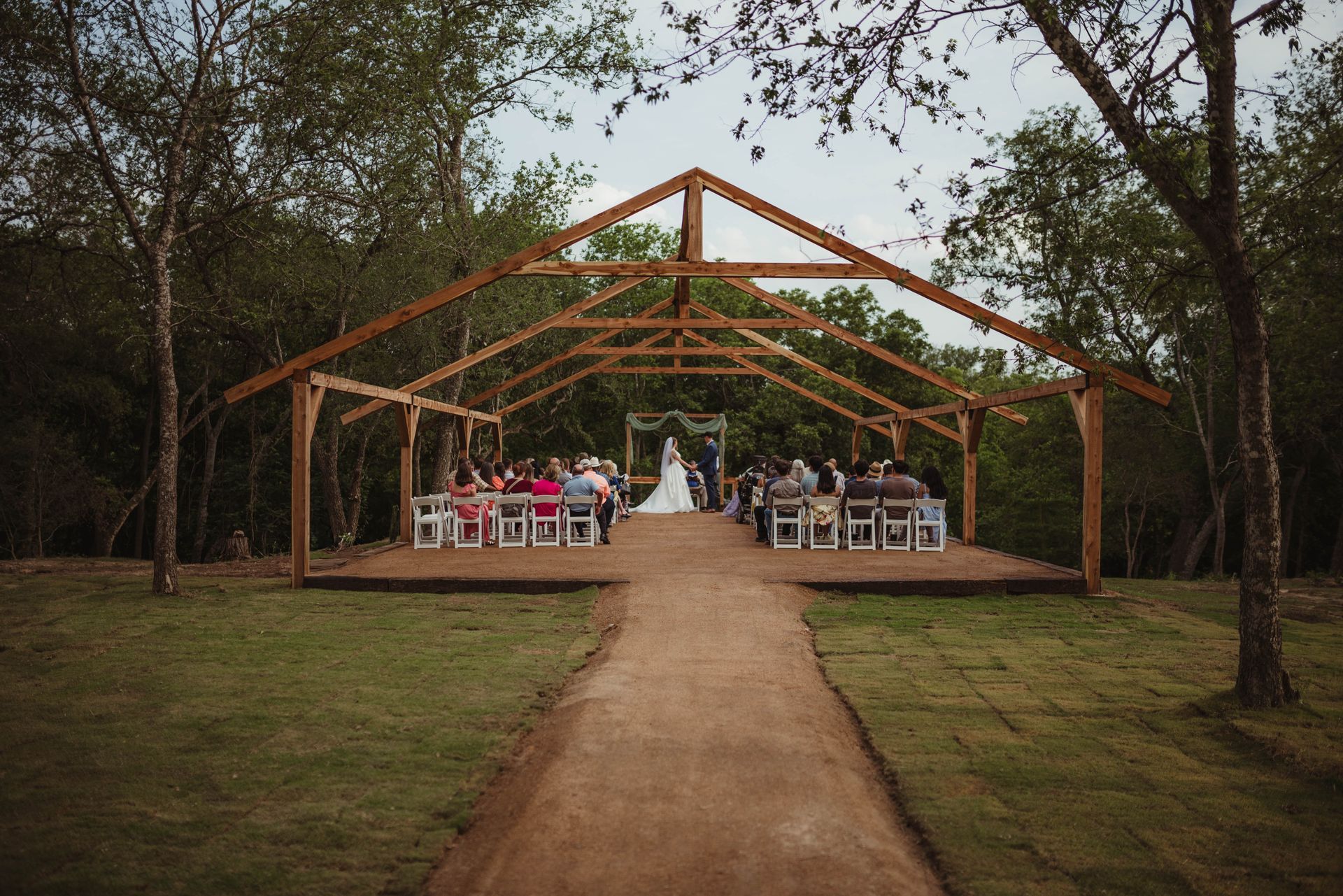 A bride and groom are getting married under a wooden structure in the woods.