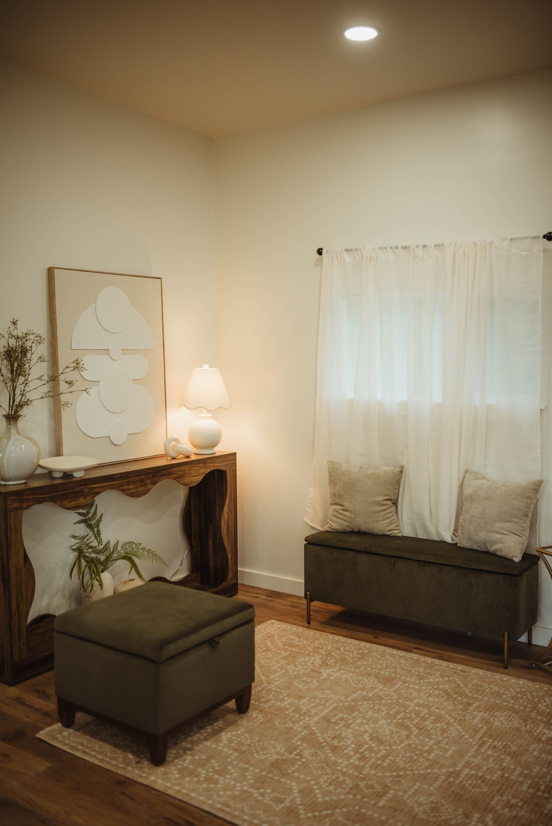 Cozy room with beige walls, wood furniture, white curtains, and a patterned rug.