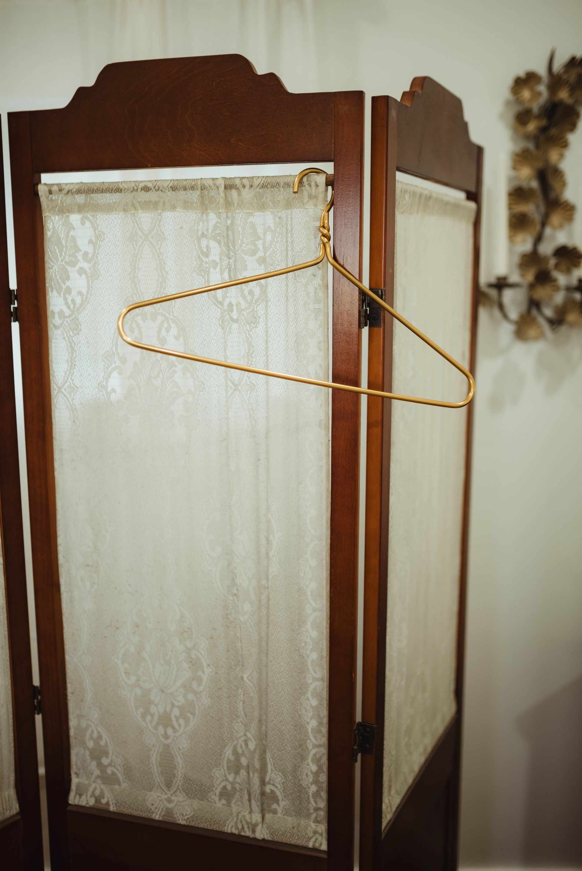 Wooden room divider with lace panels and a clothes hanger.