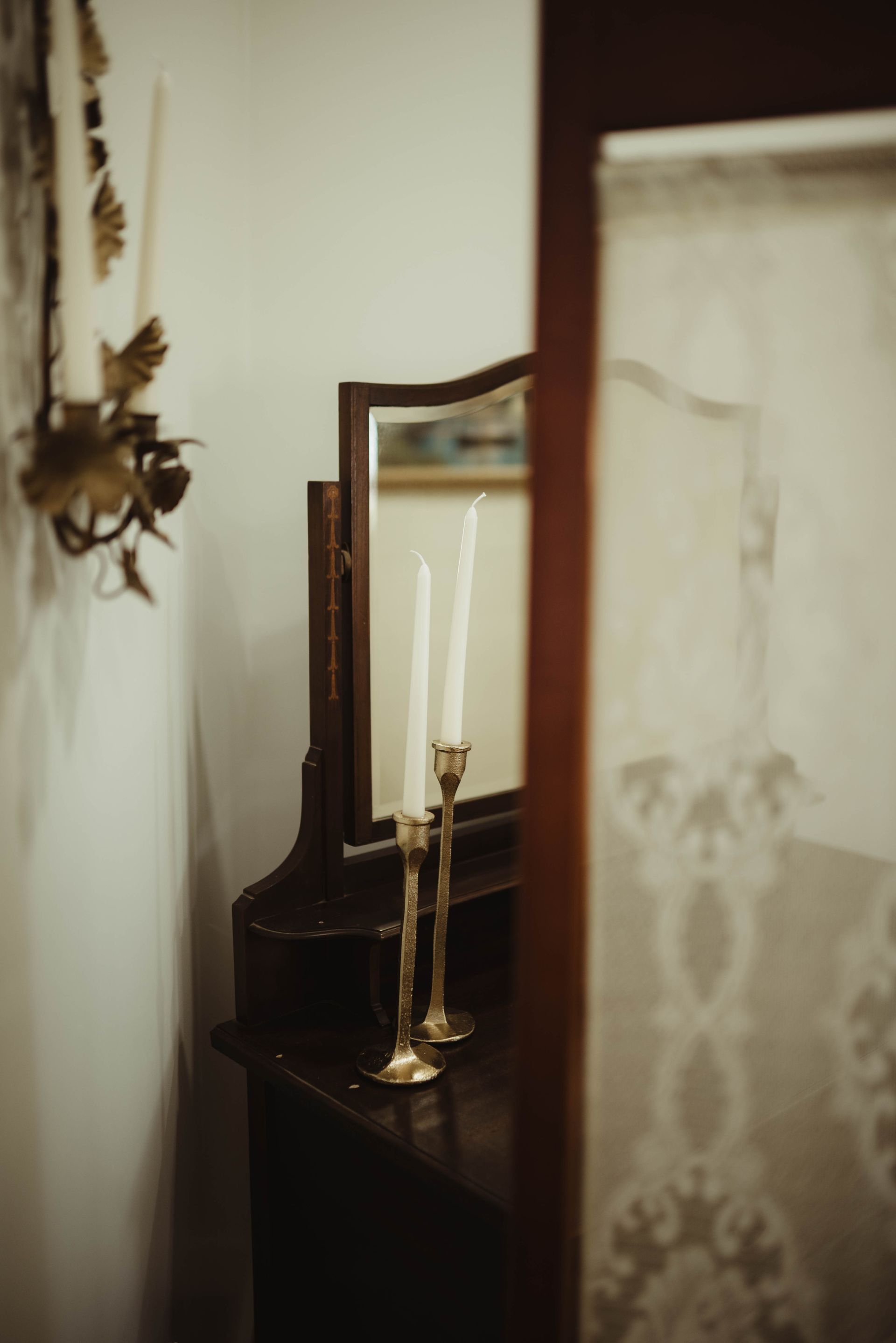 A dark wooden vanity with candles in gold holders, next to a partially visible patterned curtain.