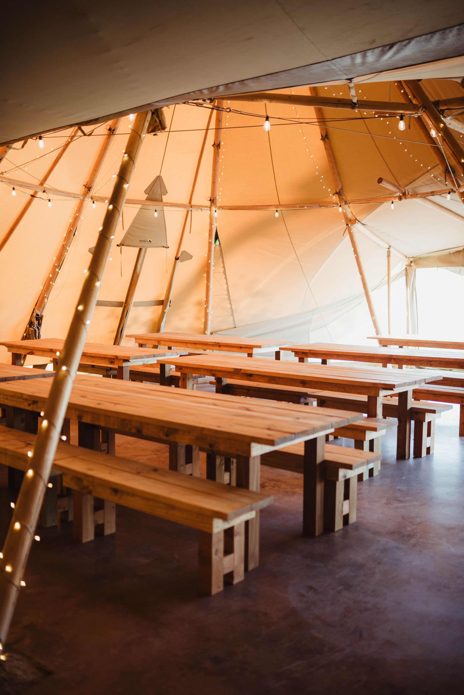 Wooden tables and benches set up inside a large, lit teepee tent.