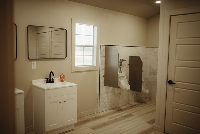 Bathroom with urinals, sink, mirror, and door. White and beige color scheme.