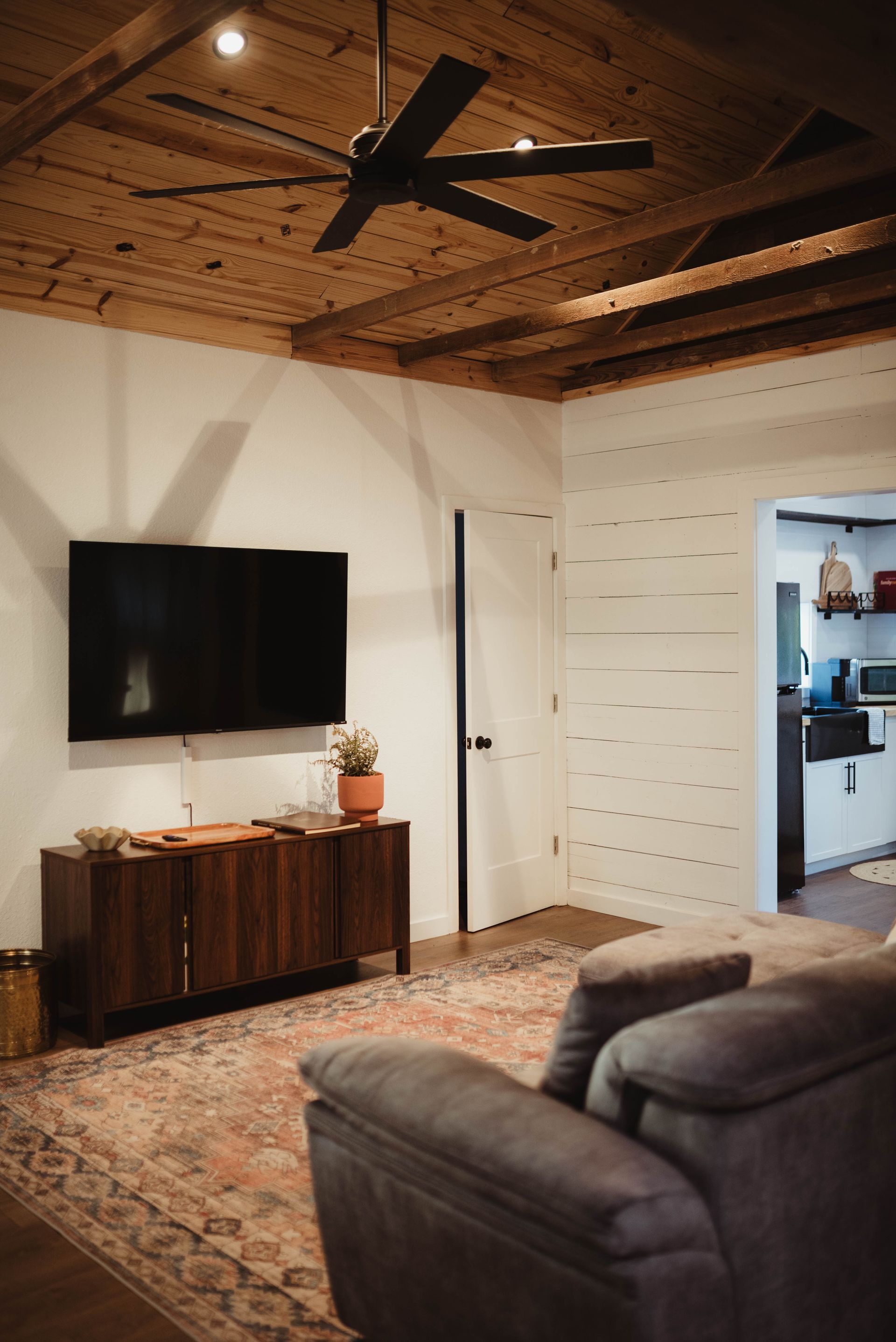 Living room with TV on a wooden cabinet, sofa on a rug, wood ceiling.