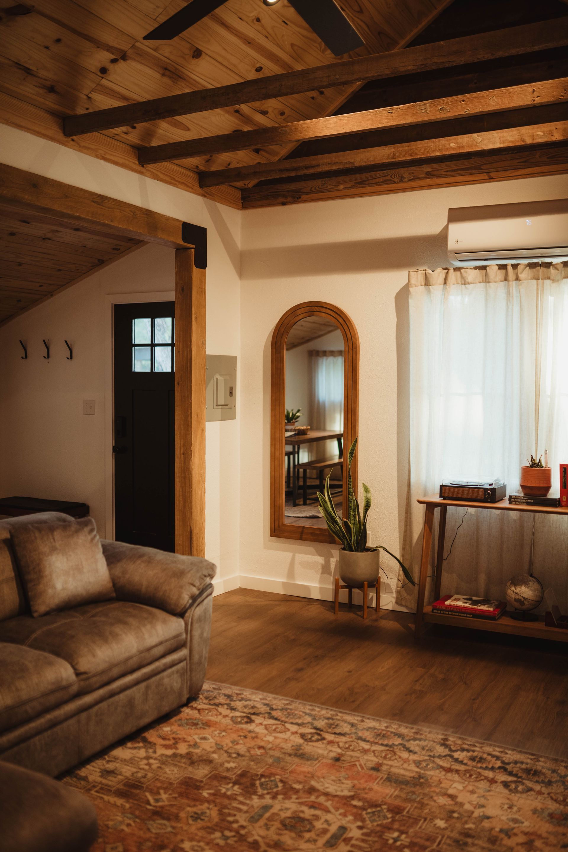 Cozy living room with a wooden ceiling, couch, rug, and large mirror.
