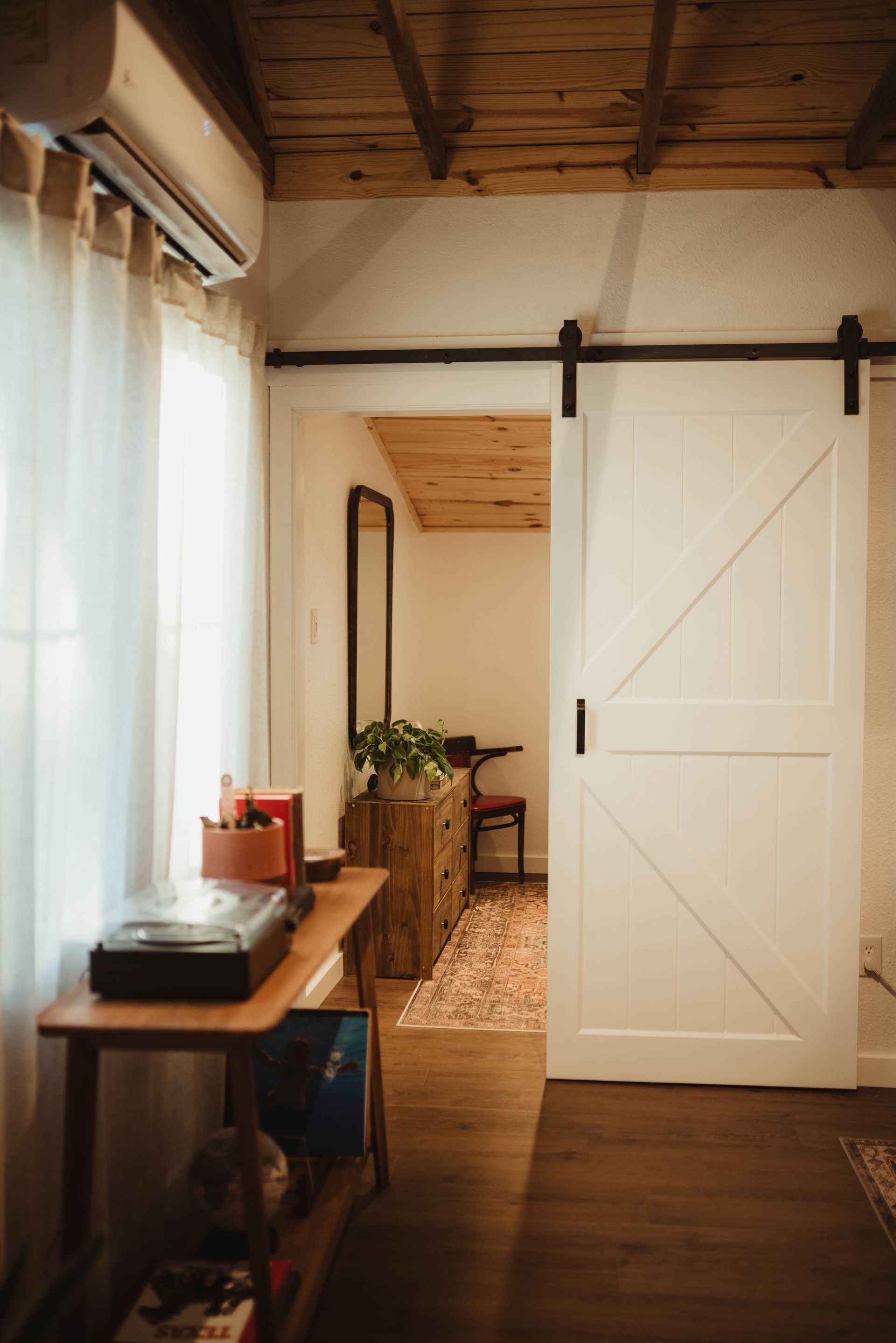 White barn door open to a room with a wooden ceiling, dresser, and a mirror.