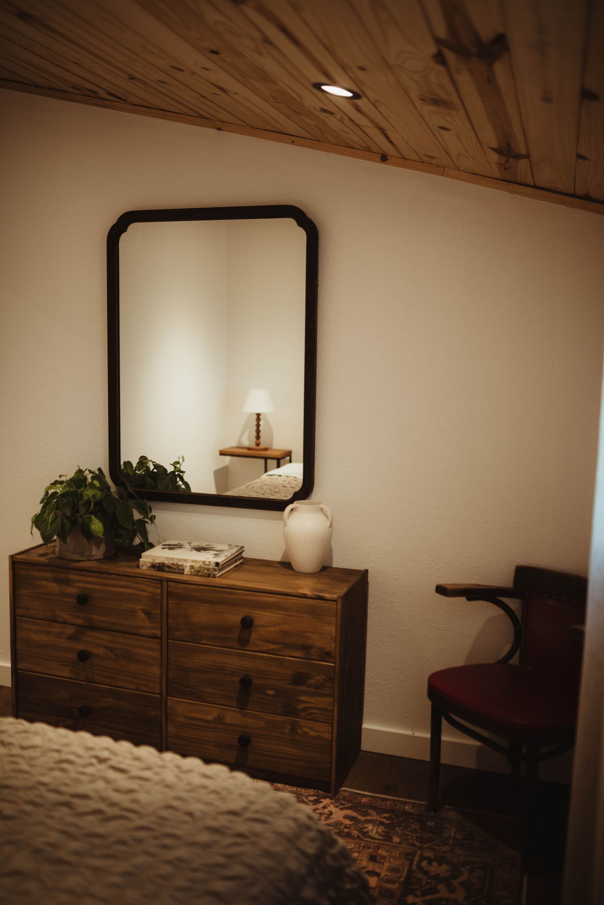 Bedroom with wooden dresser, mirror, chair, and wood ceiling; cream walls.