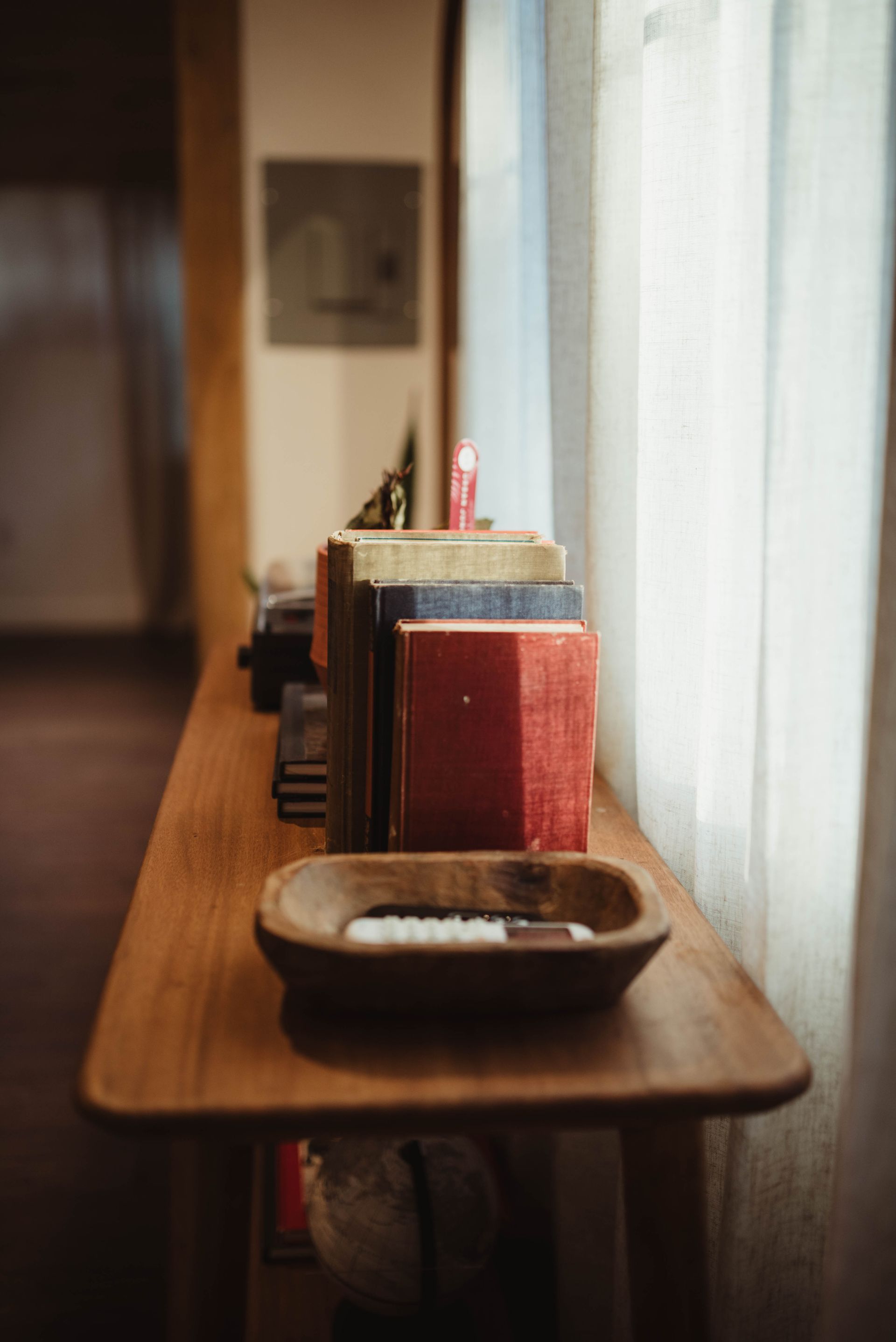 Wooden table with books, candle, and wooden bowl near a window.