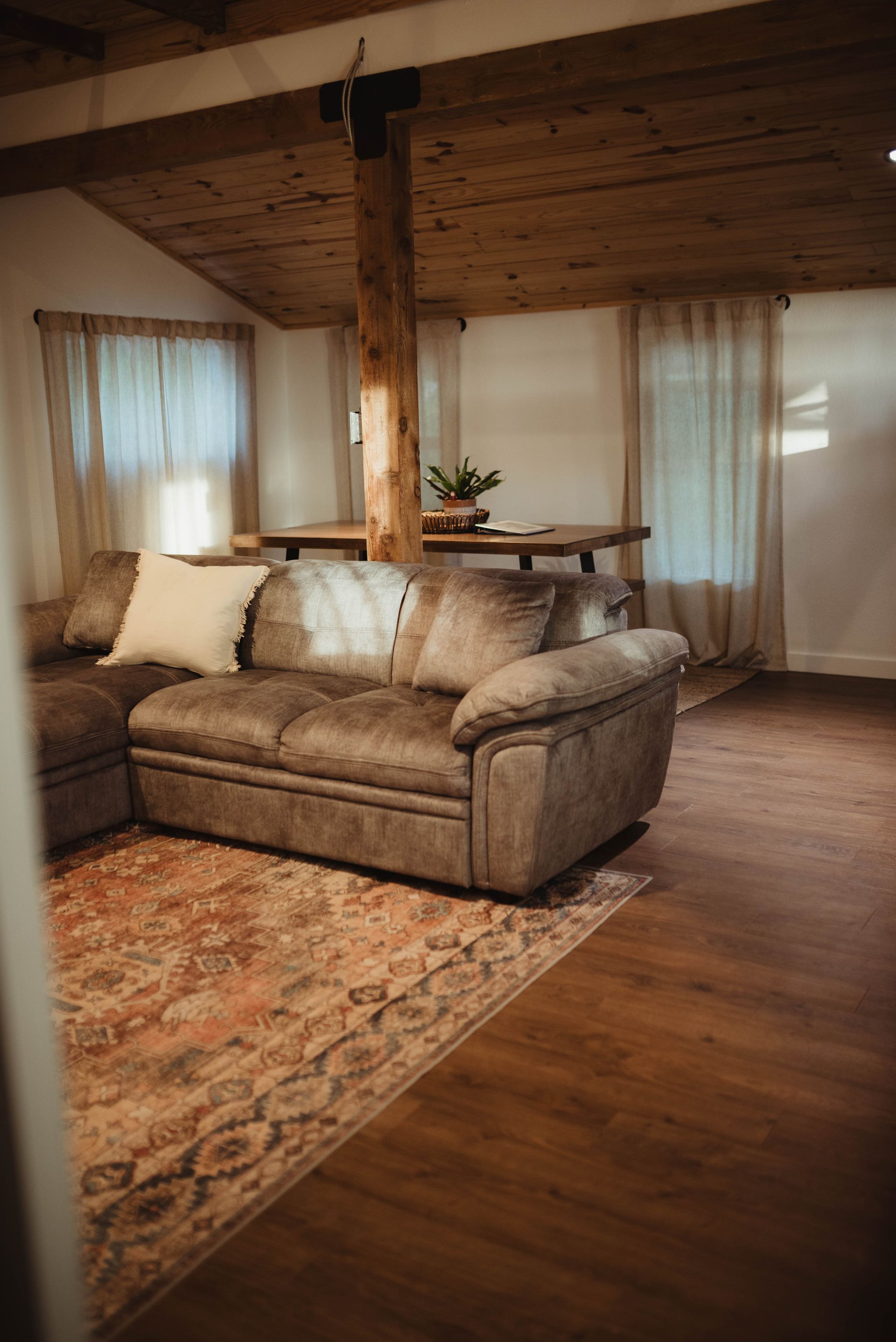 Living room with sectional sofa, rug, wooden beams, and table.