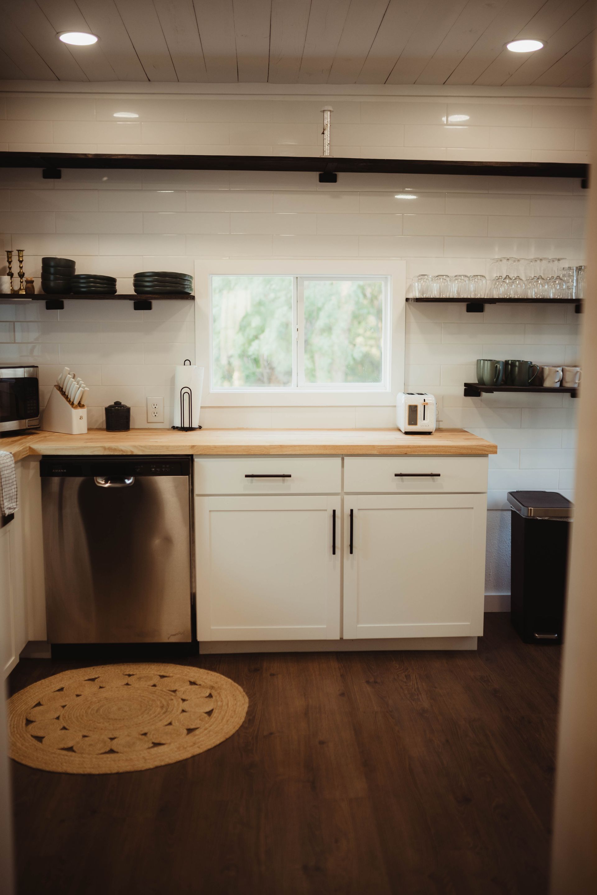 Modern white kitchen with open shelves, stainless steel appliances, and a round rug.