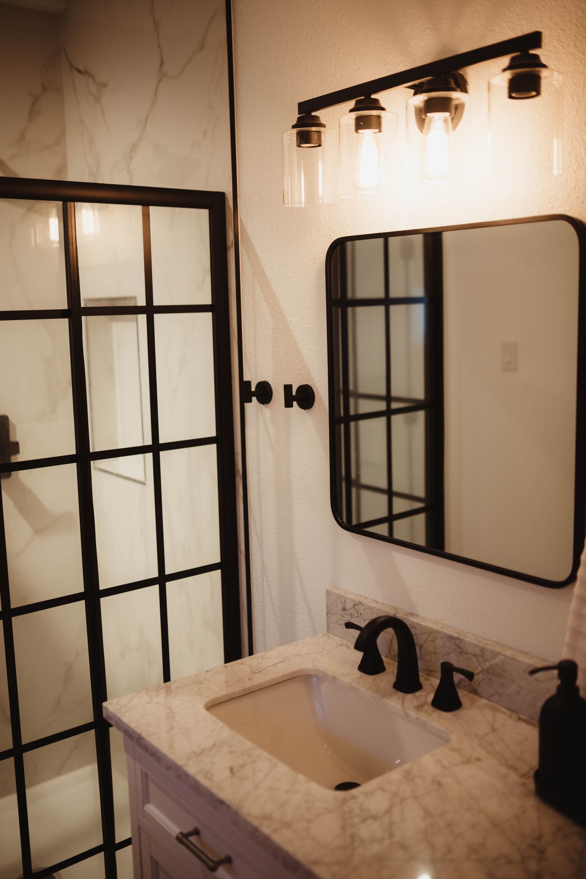 Modern bathroom with black-framed shower and mirror, white marble countertop, and black fixtures.