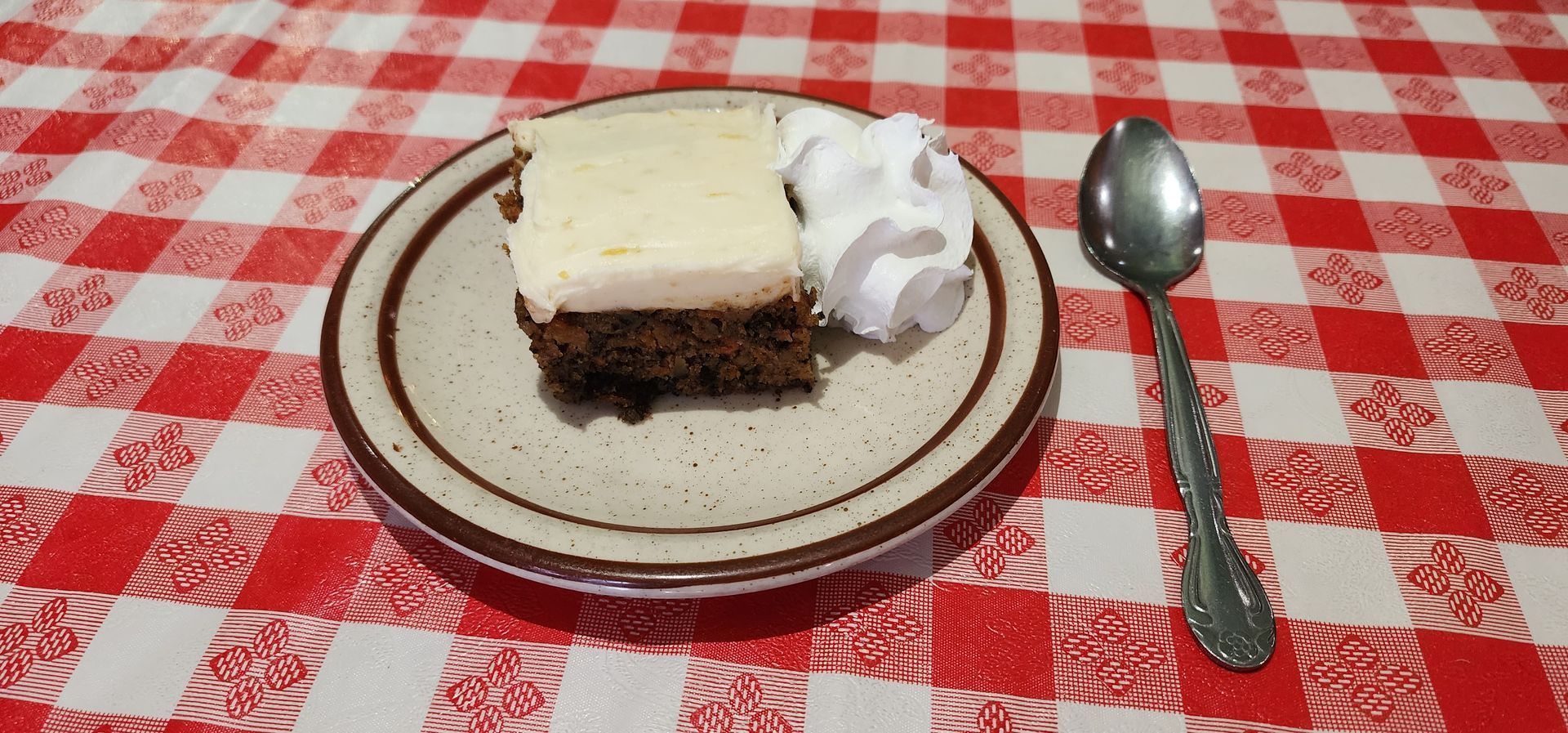 A piece of brownie with whipped cream on a plate next to a spoon