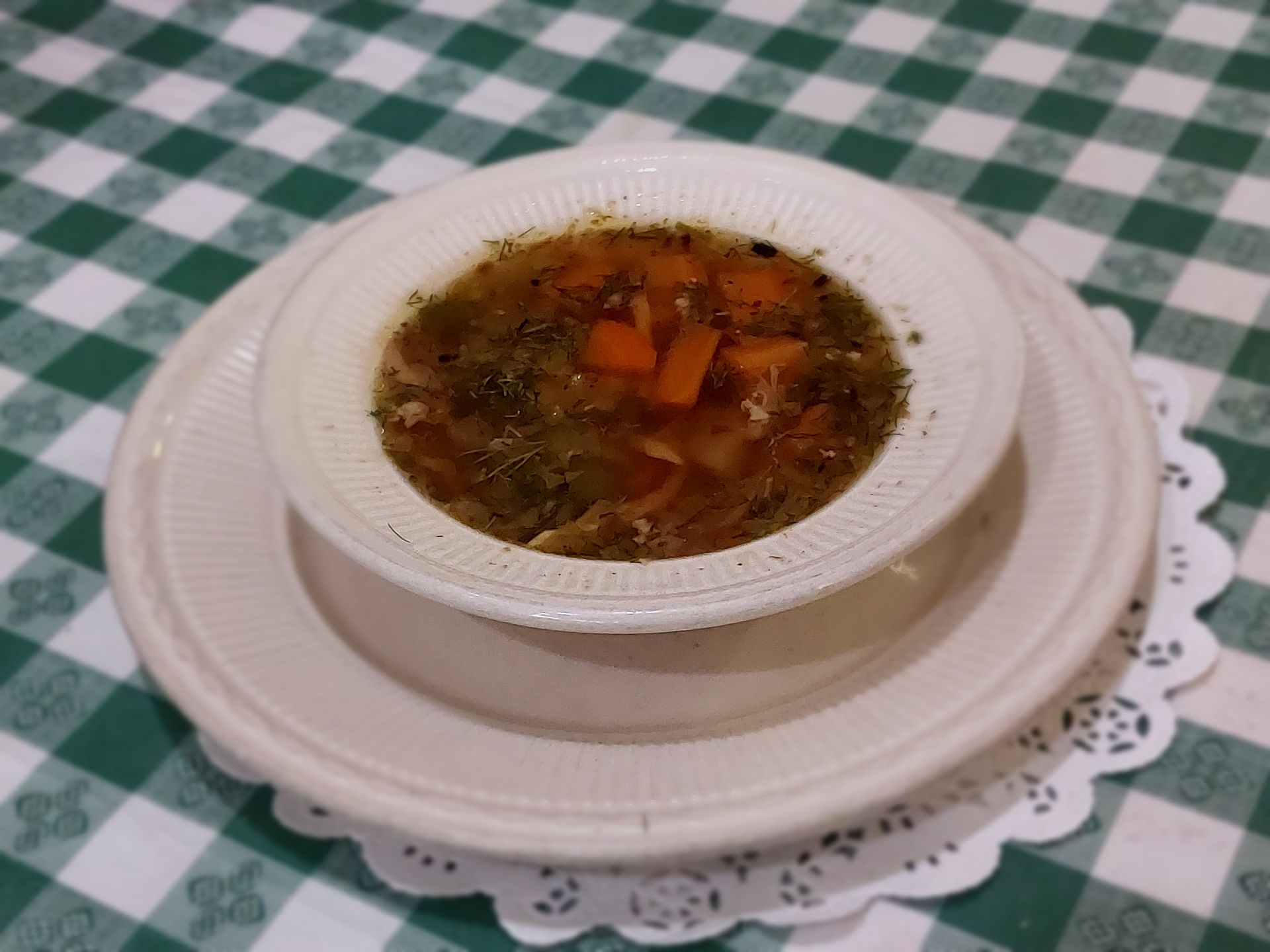 A bowl of soup on a plate on a checkered table cloth