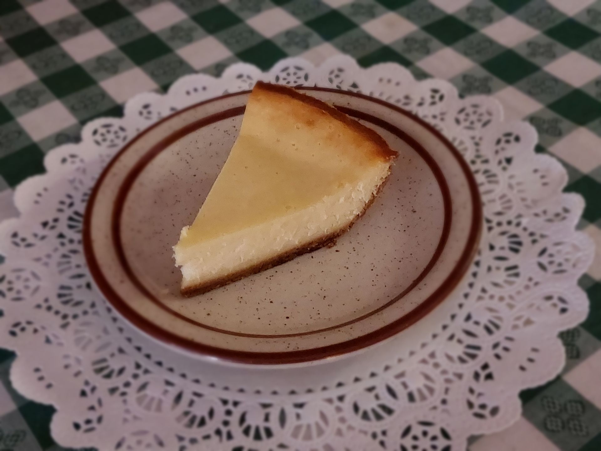 A slice of cheesecake on a plate on a checkered table cloth