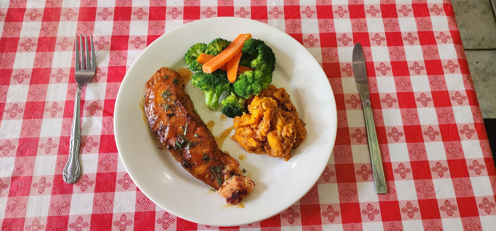 A plate of food with broccoli carrots and mashed potatoes on a checkered table cloth.