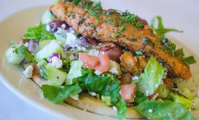 A white plate topped with a salad and a piece of meat.
