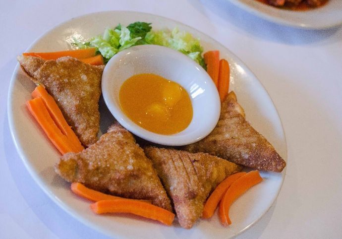 A white plate topped with fried food and carrots with a dipping sauce.